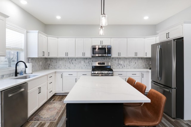 kitchen with appliances with stainless steel finishes, sink, pendant lighting, white cabinets, and a kitchen island