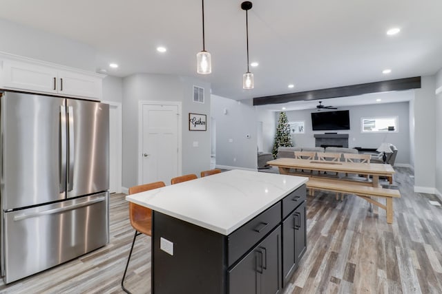 kitchen with a center island, white cabinets, hanging light fixtures, stainless steel fridge, and light hardwood / wood-style floors