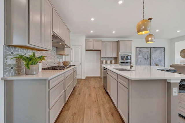 kitchen with light hardwood / wood-style flooring, backsplash, pendant lighting, a center island with sink, and appliances with stainless steel finishes