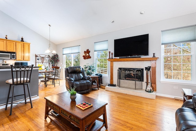 living room featuring a tile fireplace, light wood-type flooring, a chandelier, and vaulted ceiling