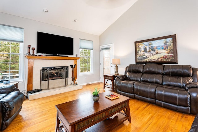 living room featuring a tile fireplace, high vaulted ceiling, and light hardwood / wood-style flooring