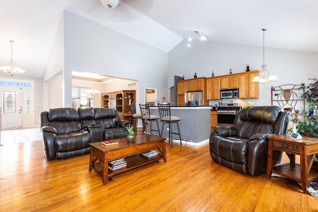 living room featuring ceiling fan with notable chandelier, light wood-type flooring, and high vaulted ceiling