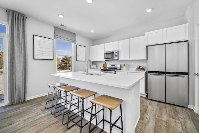 kitchen with a center island with sink, white cabinets, sink, hardwood / wood-style flooring, and stainless steel appliances