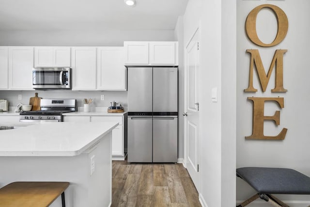 kitchen featuring white cabinets, stainless steel appliances, a breakfast bar area, and dark wood-type flooring