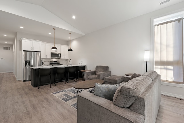 living room featuring light wood-type flooring, sink, and vaulted ceiling