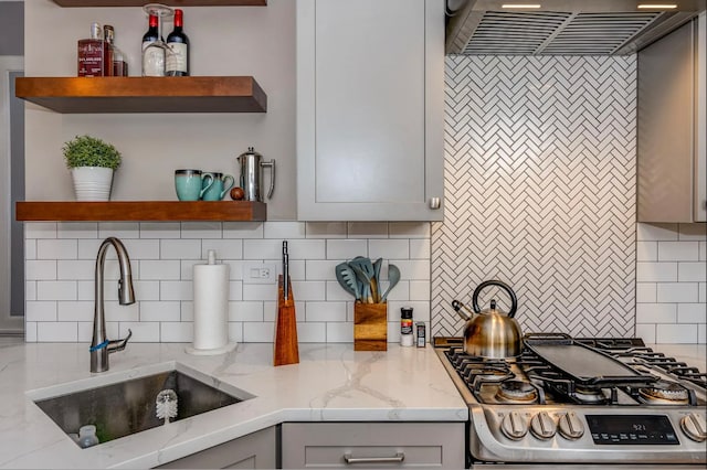 kitchen featuring stove, premium range hood, sink, light stone countertops, and tasteful backsplash