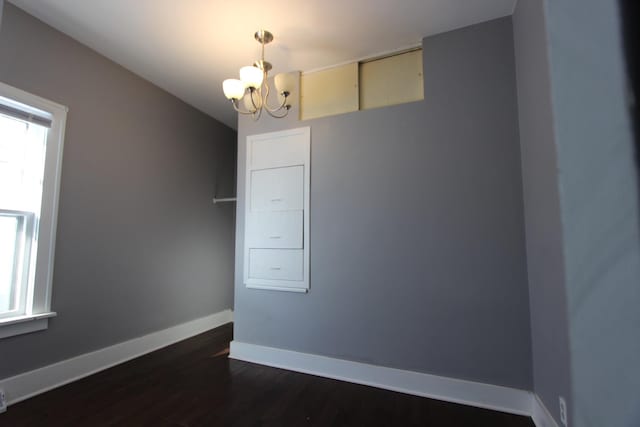 empty room with dark hardwood / wood-style flooring and an inviting chandelier