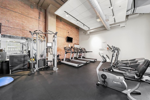 exercise room with a high ceiling, track lighting, and brick wall