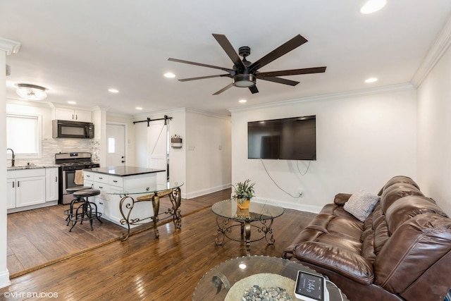 living room with dark wood-type flooring, sink, ceiling fan, a barn door, and ornamental molding