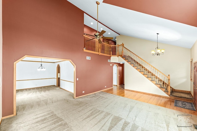 unfurnished living room featuring ceiling fan with notable chandelier, carpet floors, and high vaulted ceiling