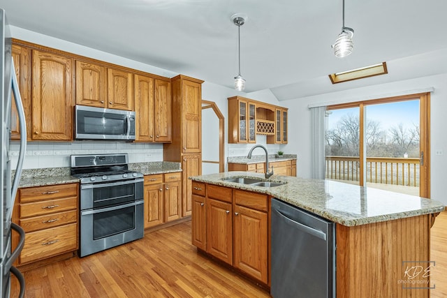 kitchen with decorative backsplash, light stone counters, stainless steel appliances, sink, and an island with sink