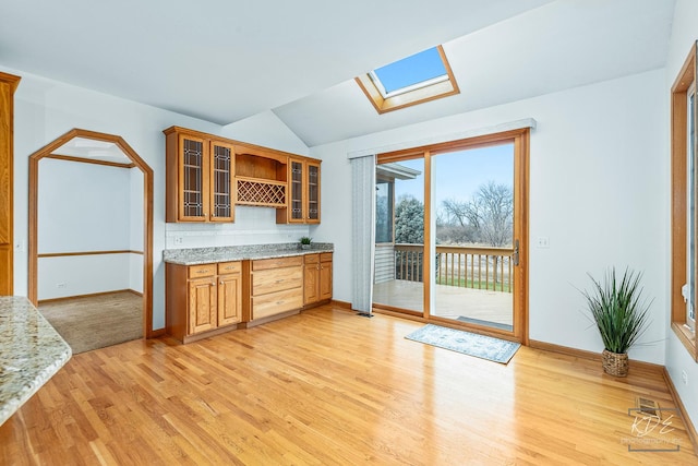 kitchen with light stone countertops, lofted ceiling with skylight, and light wood-type flooring