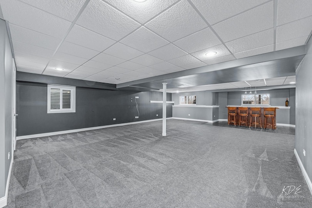 basement with a paneled ceiling, dark carpet, and indoor bar