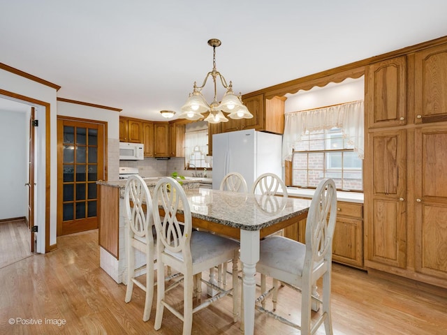 dining room with sink, light wood-type flooring, ornamental molding, and a chandelier