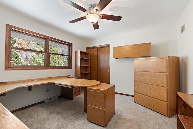 unfurnished office with ceiling fan, light colored carpet, and built in desk