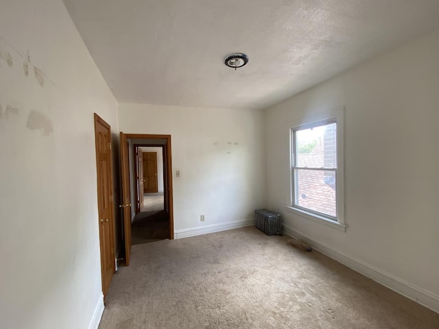 unfurnished room with carpet, radiator heating unit, and a textured ceiling