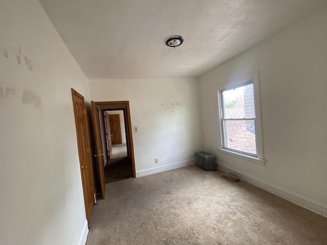 carpeted spare room featuring a textured ceiling, radiator heating unit, and vaulted ceiling