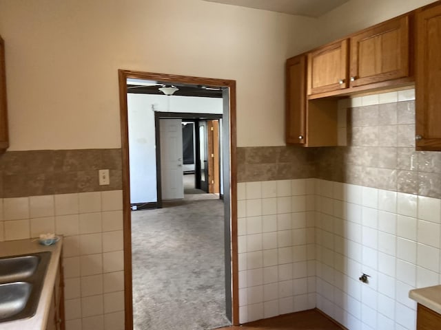 kitchen featuring carpet flooring, ceiling fan, sink, and tile walls