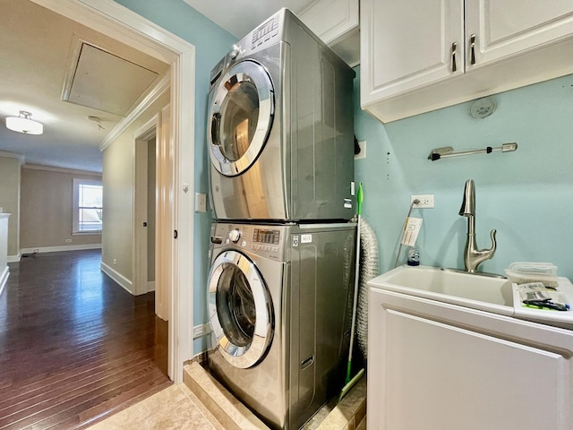 laundry room with cabinets, sink, hardwood / wood-style flooring, ornamental molding, and stacked washer / dryer