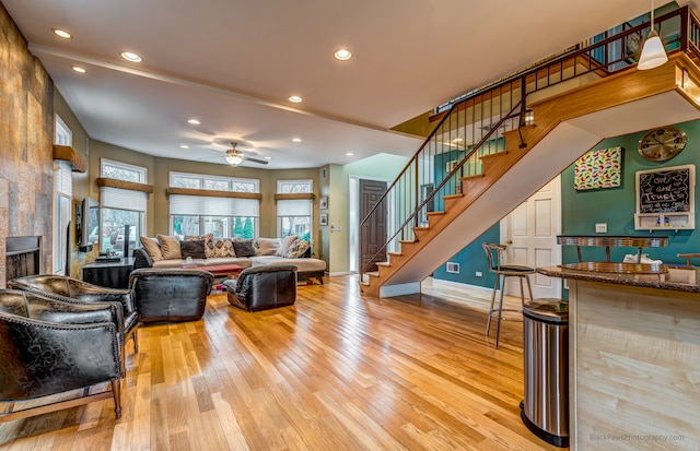 living room featuring ceiling fan, light wood-type flooring, and a tiled fireplace