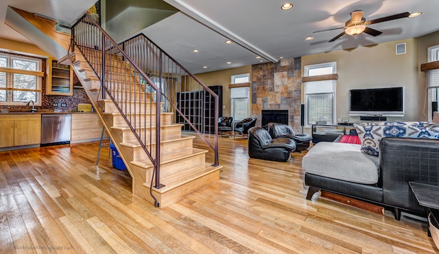 living room with ceiling fan, sink, light hardwood / wood-style flooring, and a tiled fireplace