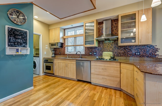 kitchen with appliances with stainless steel finishes, light brown cabinetry, washer / dryer, and wall chimney range hood