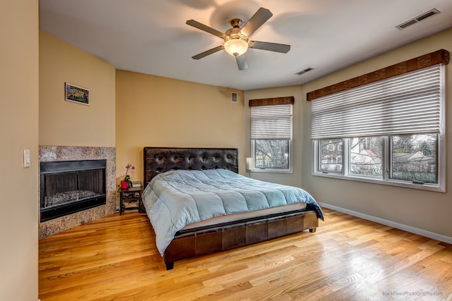 bedroom featuring light hardwood / wood-style flooring, ceiling fan, and a tiled fireplace