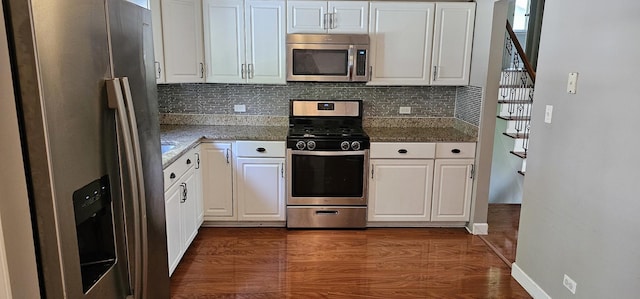 kitchen with appliances with stainless steel finishes, tasteful backsplash, dark wood-type flooring, dark stone countertops, and white cabinets