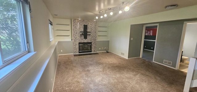 unfurnished living room with carpet, built in shelves, rail lighting, and a fireplace