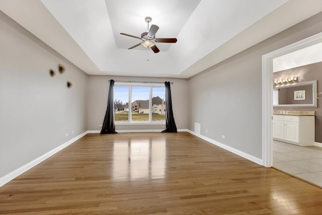 empty room featuring a tray ceiling, ceiling fan, light hardwood / wood-style flooring, and sink