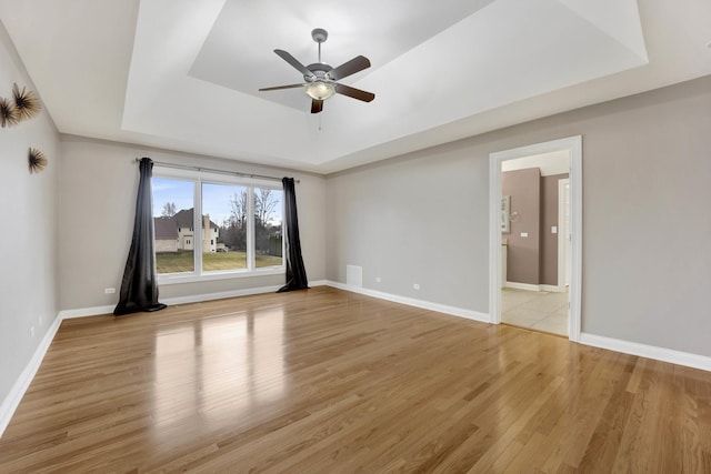 spare room with ceiling fan, light hardwood / wood-style floors, and a tray ceiling