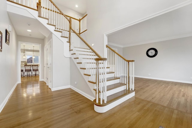 staircase featuring a high ceiling, hardwood / wood-style flooring, and ornamental molding