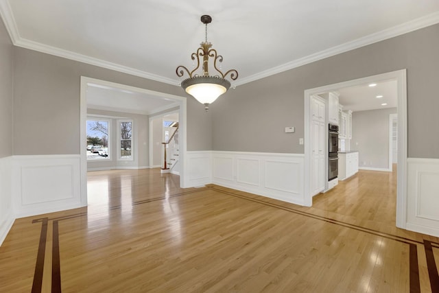 unfurnished dining area featuring light wood-type flooring, crown molding, and a chandelier