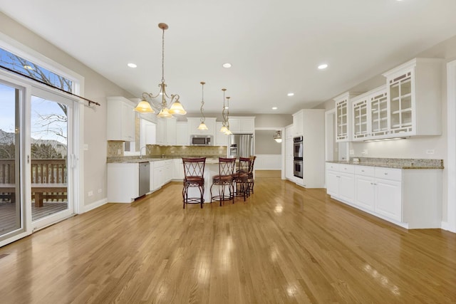 kitchen with appliances with stainless steel finishes, a kitchen breakfast bar, decorative light fixtures, a center island, and white cabinetry