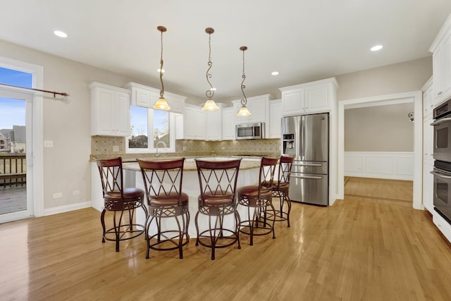 kitchen featuring white cabinets, stainless steel appliances, hanging light fixtures, and light hardwood / wood-style flooring