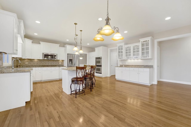 kitchen featuring hanging light fixtures, light wood-type flooring, a kitchen island, white cabinetry, and stainless steel appliances