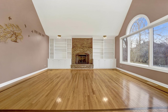 unfurnished living room featuring built in shelves, vaulted ceiling, light hardwood / wood-style flooring, and a brick fireplace