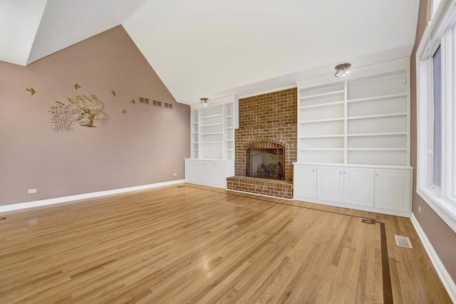 unfurnished living room featuring built in shelves, light hardwood / wood-style floors, vaulted ceiling, and a brick fireplace