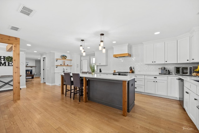 kitchen with a kitchen island, white cabinets, stainless steel dishwasher, and pendant lighting