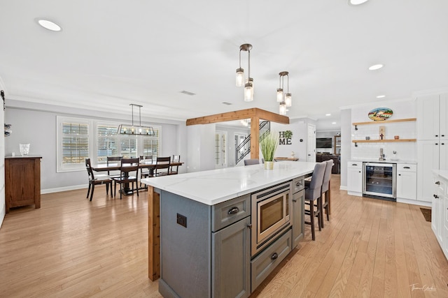 kitchen featuring wine cooler, hanging light fixtures, light stone counters, stainless steel microwave, and white cabinets