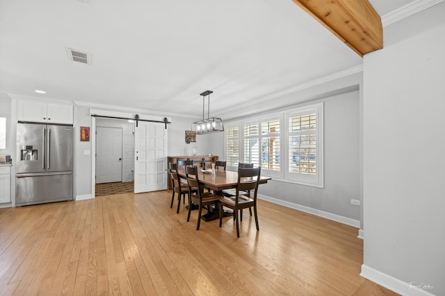 dining space with ornamental molding, light wood-type flooring, and a barn door