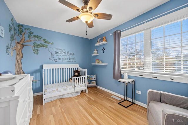 bedroom featuring a nursery area, light wood-type flooring, and ceiling fan