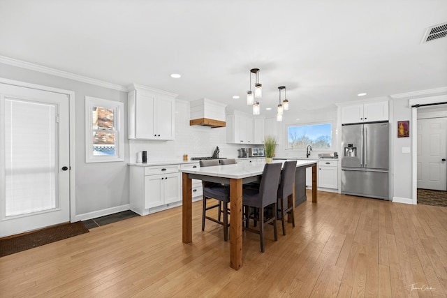 kitchen featuring high quality fridge, a kitchen island, decorative light fixtures, and white cabinetry