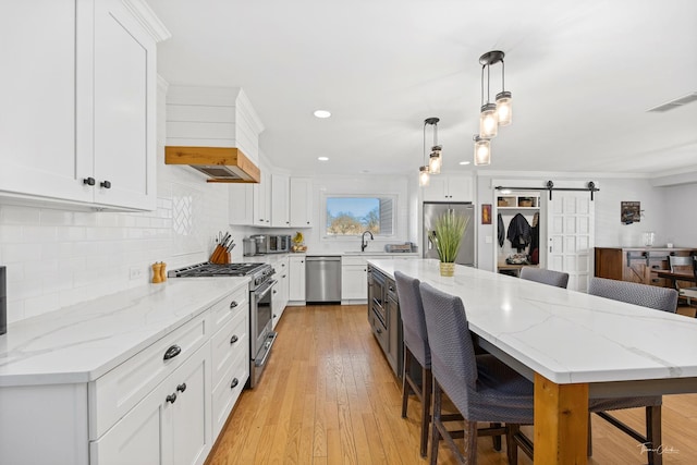 kitchen with appliances with stainless steel finishes, white cabinetry, and a barn door