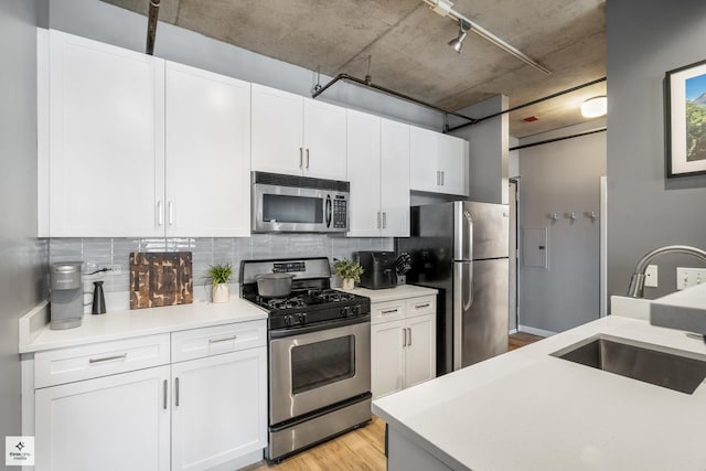 kitchen featuring white cabinetry, sink, light hardwood / wood-style floors, decorative backsplash, and appliances with stainless steel finishes