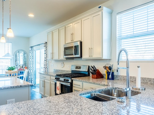 kitchen with sink, light stone counters, hanging light fixtures, and stainless steel appliances