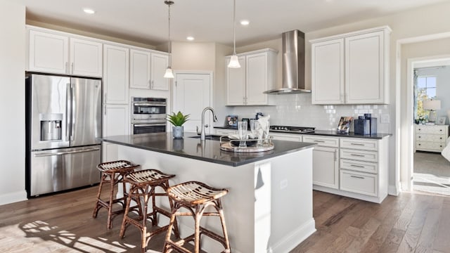 kitchen with an island with sink, a breakfast bar area, stainless steel appliances, wall chimney exhaust hood, and white cabinets