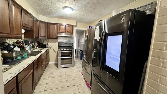 kitchen with range with two ovens, tile countertops, light tile patterned floors, fridge, and decorative backsplash