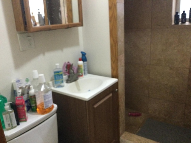 bathroom with toilet, a tile shower, and vanity