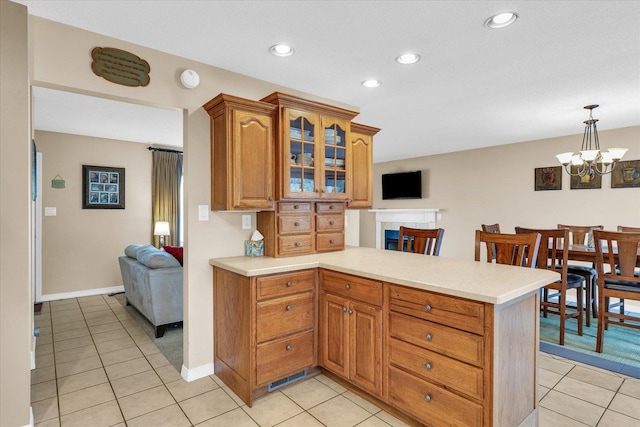 kitchen with kitchen peninsula, pendant lighting, a notable chandelier, and a tiled fireplace